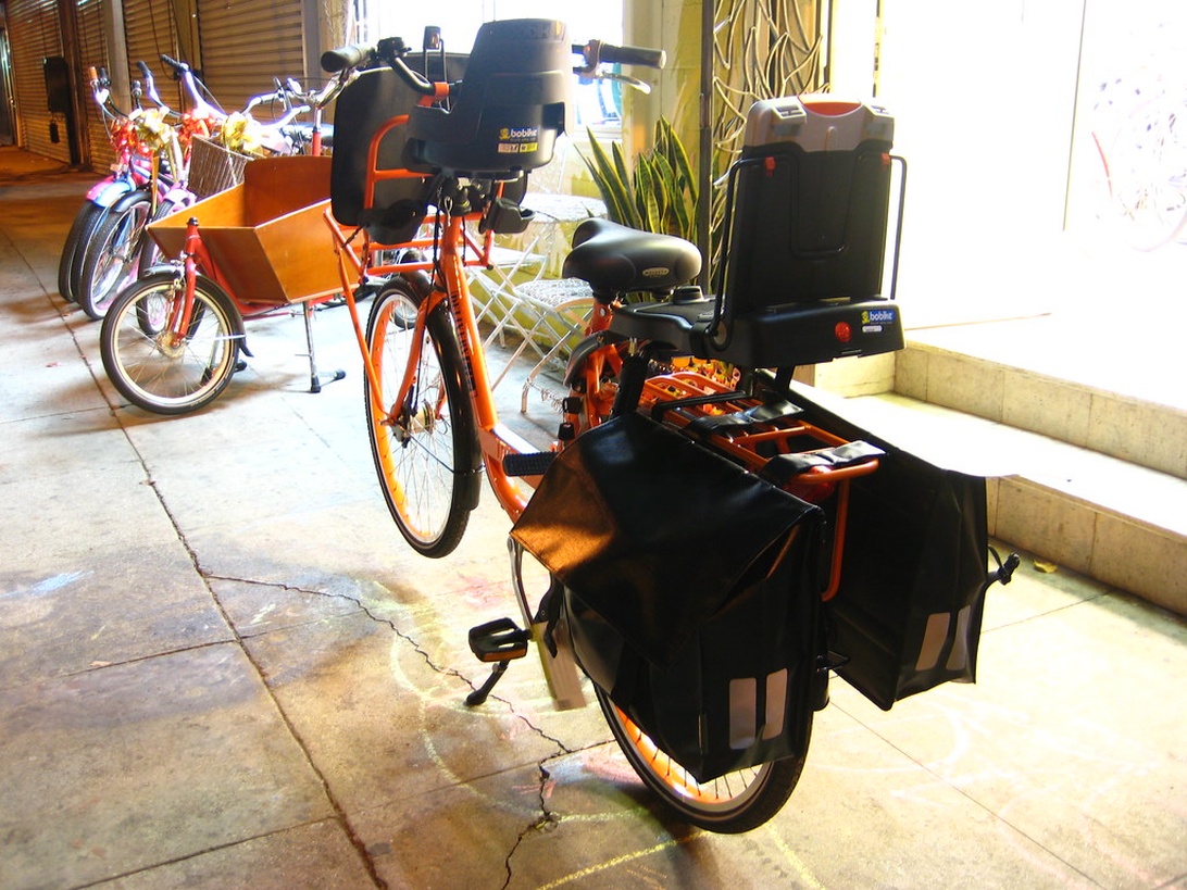 Oranje bezorgfiets met diverse transportkoffers en fietstassen.